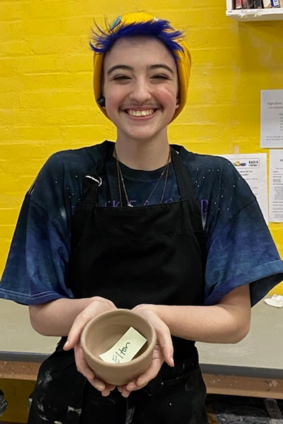 A student displays an unfired ceramic bowl
